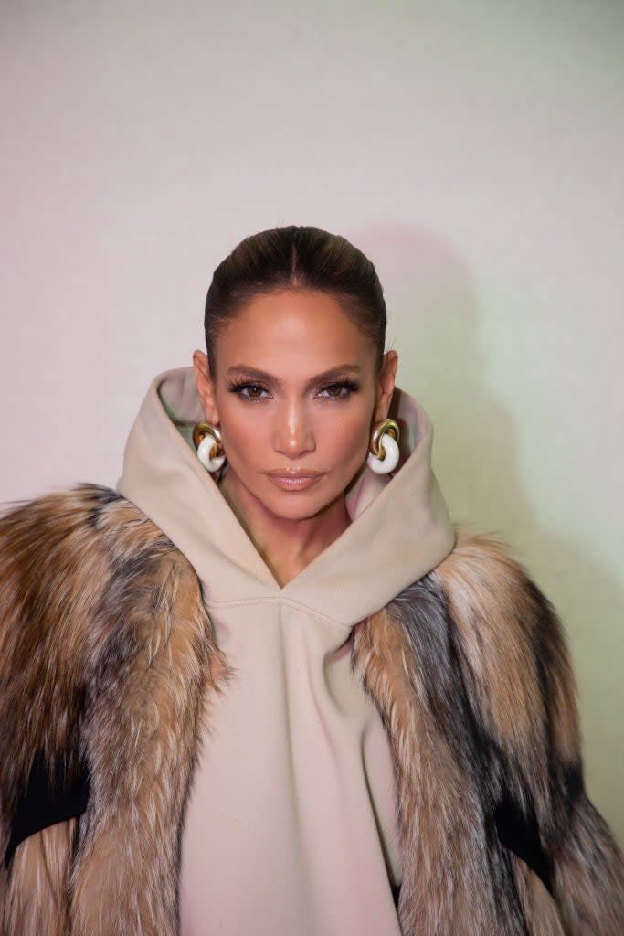 Jennifer Lopez wears a hooded beige outfit with a fur accent and large hoop earrings