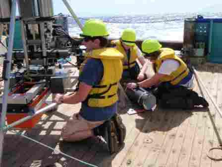 Preparing the Hadal Lander. Alan Jamieson (left) sets up the camera, while Niki Lacey (centre) and Heather Ritchie (right) (both PhD students at the University of Aberdeen) secure an amphipod trap to the leg of the lander. Photo credit: NIWA/University of Aberdeen.