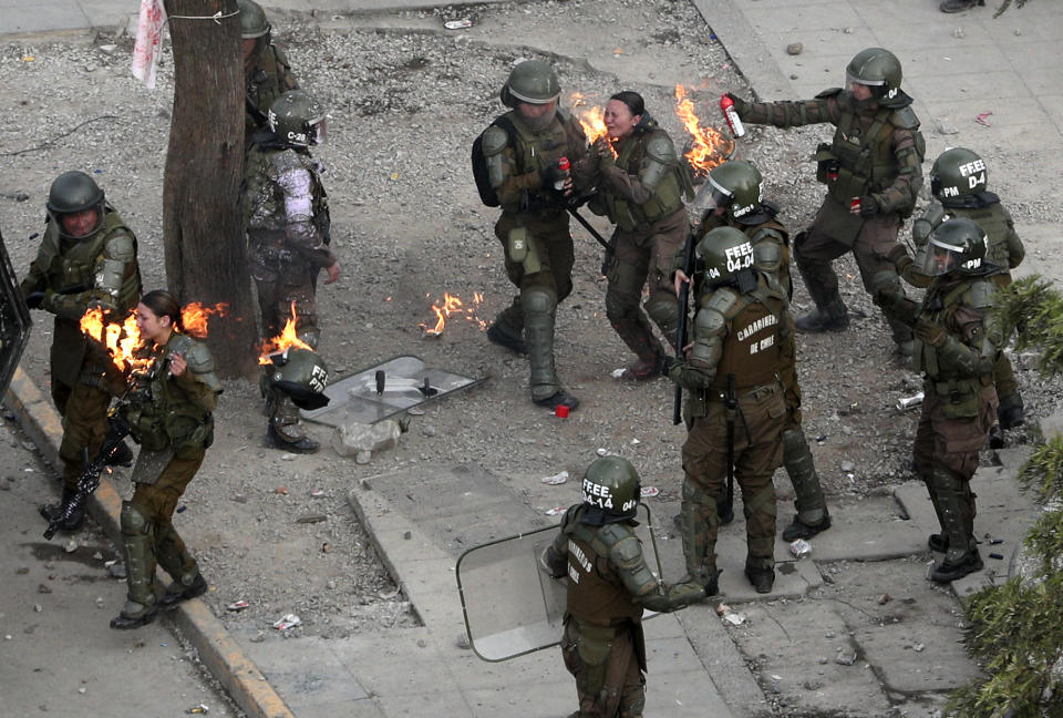 Police officers run to get assistance after being hit with a gasoline bomb thrown by protesters during an anti-government protest in Santiago, Chile, Monday, Nov. 4, 2019. Chile has been facing weeks of unrest, triggered by a relatively minor increase in subway fares. The protests have shaken a nation noted for economic stability over the past decades, which has seen steadily declining poverty despite persistent high rates of inequality. (AP Photo/Esteban Felix)