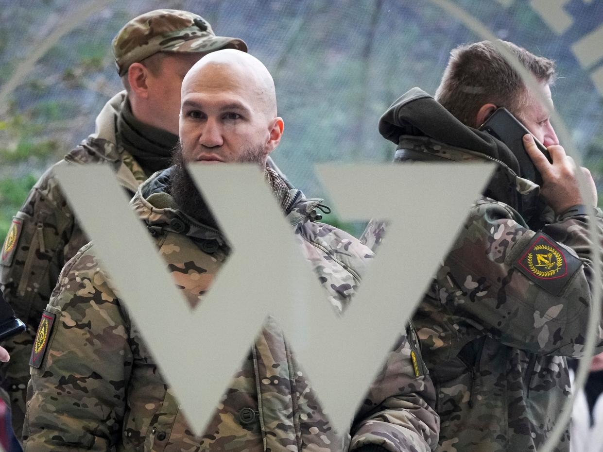 Men dressed in Russian military fatigues stand in front of a door with a giant W in front of it.