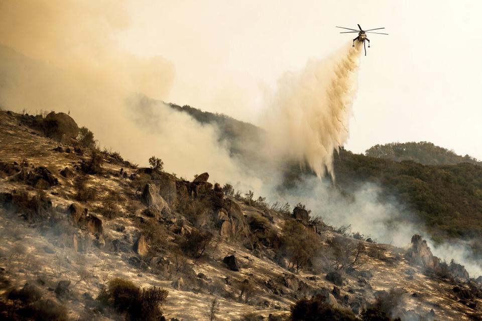 A helicopter drops water on a wildfire.