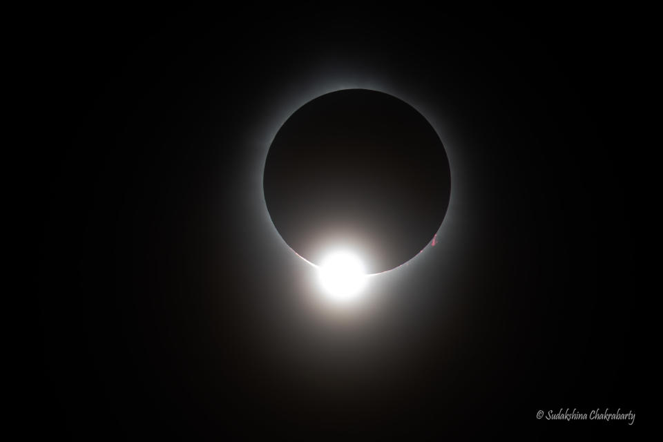 an eclipsed sun appears as a black circle with a hazy white outline and a bright white circular shape at the lower edge which makes the scene look like a diamond ring.