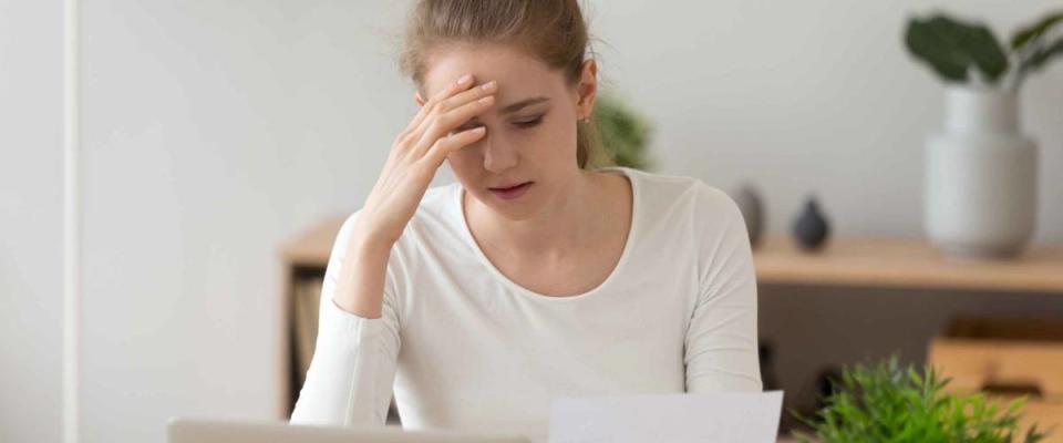 Unhappy young woman looking at letter, hand to her forehead.