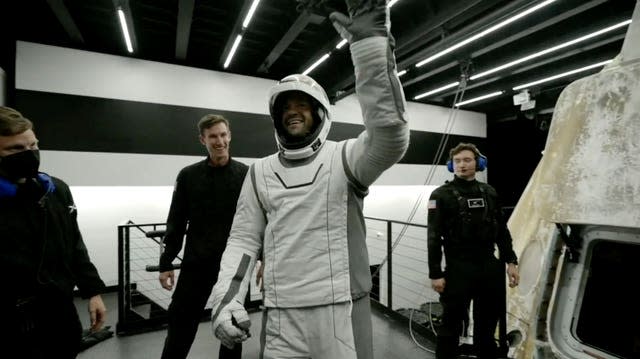 A man in a spacesuit waves 