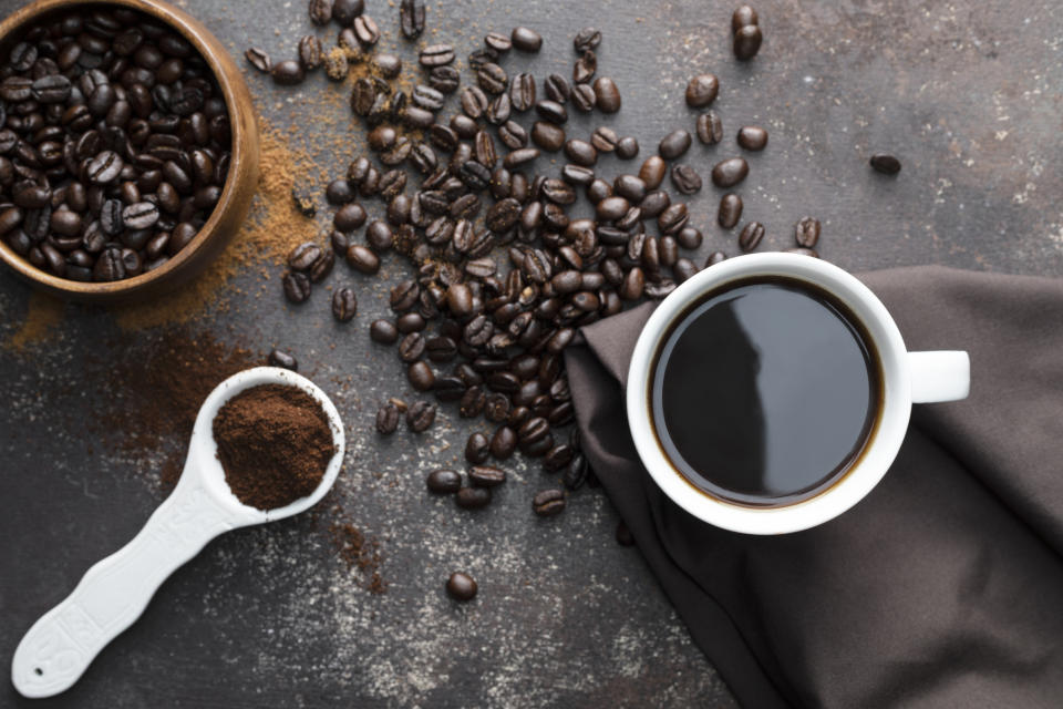 Direct above view of roasted coffee beans, white coffee cup with black coffee, dark brown colored napkin with one white spoon full with blended coffee