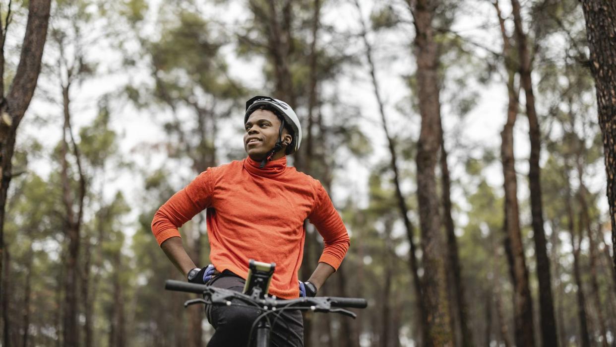 handsome african american man with a mountain bike standing in the forest, while looking around