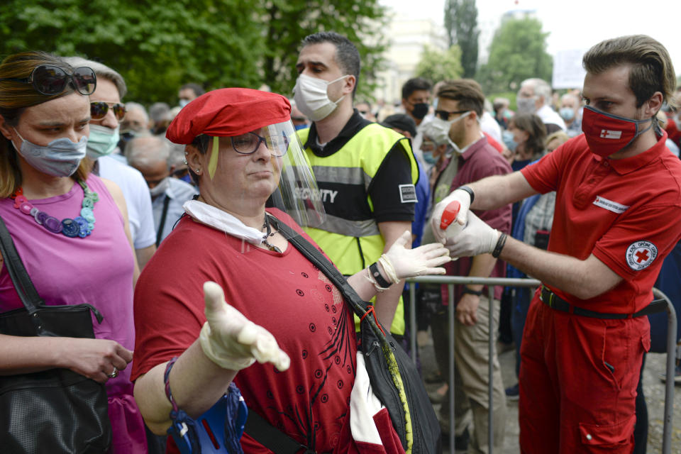 A woman gets her hands sprayed with disinfectant before joining an anti-Nazi protest outside the Sacred Heart Cathedral during a mass commemorating members of the pro-Nazi Croatian WWII Ustasha regime, responsible for sending tens of thousands of Serbs, Gypsies and Jews to their death in concentration camps, who were killed at the end of WWII by Yugoslav communist troops, in Sarajevo, Bosnia, Saturday, May 16, 2020. Bosnian Catholic clerics along with Croatian state representatives and members of the Bosnian Croats community attended a religious service commemorating the massacre of Croatian pro-Nazis by victorious communists at the end of World War II. (AP Photo/Kemal Softic)