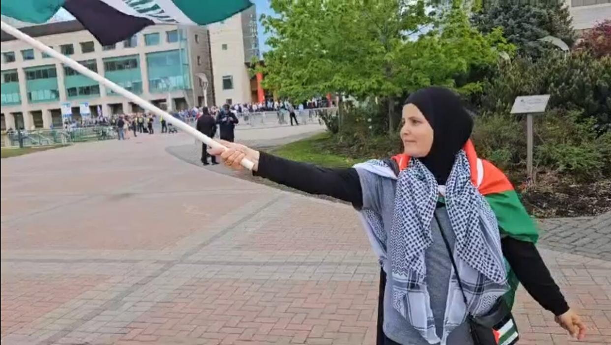 A screenshot of a video showing Hayfa Abdelkhaleq waving a Palestinian flag outside of city hall during a flag-raising ceremony in honour of Israel's Independence Day. Moments later, a person walks up to Abdelkhaleq and pulls off her hijab. (Submitted by Hayfa Abdelkhaleq - image credit)