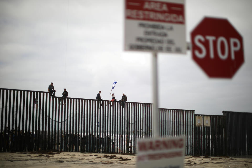 People&nbsp;sit on the top of the U.S.-Mexico border wall.