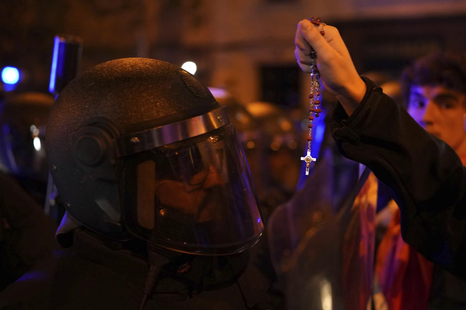 A demonstrator holds a rosary next to a police officer during a protest against the amnesty at the headquarters of Socialist party in Madrid, Spain, Saturday, Nov. 11, 2023. Protests backed by Vox party turned on Saturday night as Spain's Socialists to grant amnesty to Catalan separatists in exchange for support of new government. (AP Photo/Joan Mateu Parra)