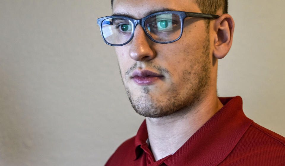 In this Sept. 20, 2021, photo Austin Moody poses for a photo as he sits a his home work station in Tampa, Fla. Moody, the Michigan native, got a scholarship from the Department of Defense that required working for the agency at least a year after graduating. Moody said he understands that state governments don't have the kind of money that federal agencies or private companies spend on recruiting and generous salaries. (AP Photo/Steve Nesius)