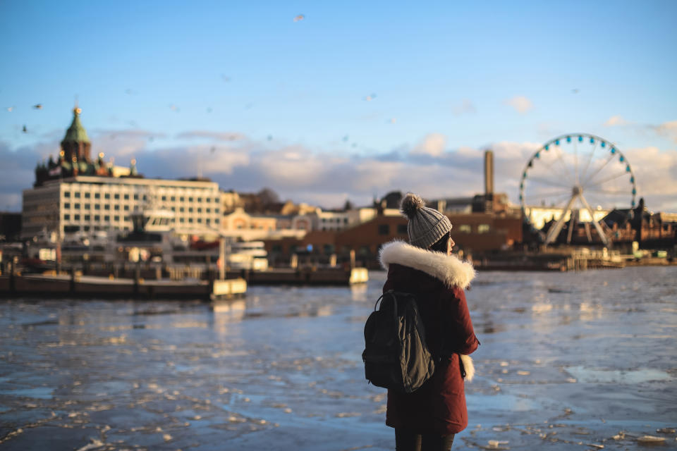 Young woman standing in front of SkyWheel Helsinki with skyline of Uspenski Orthodox Cathedral and Alvar Aalto’s Enso-Gutzeit Headquarters at dawn, South Harbour, Kauppatori, Helsinki, capital city of Finland.