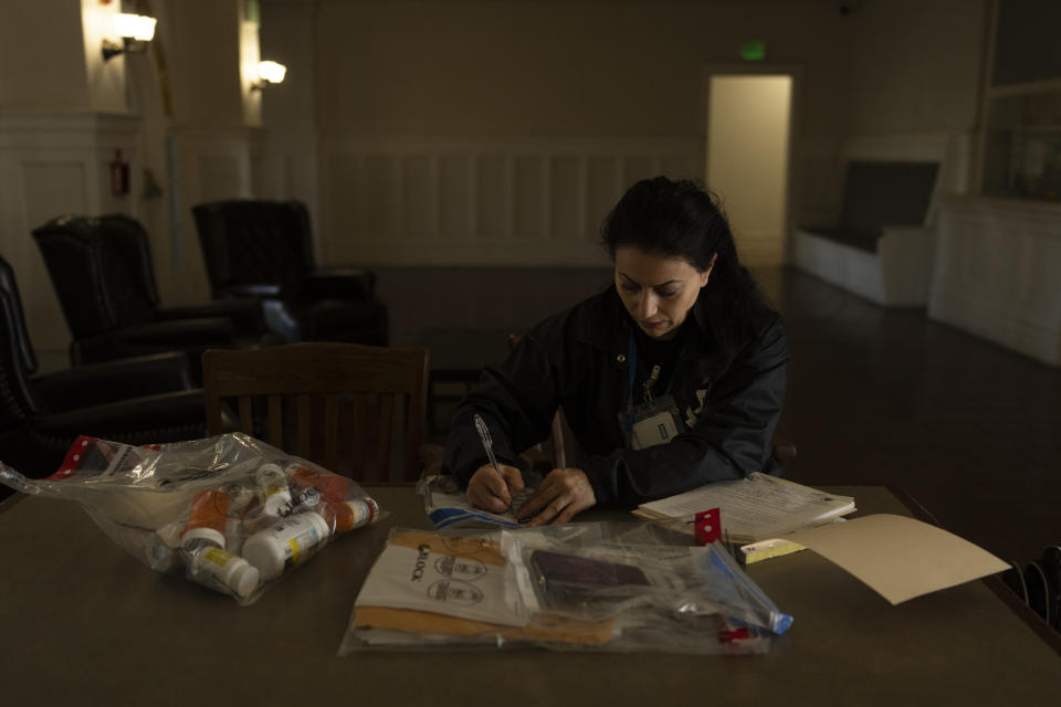 Arusyak Martirosyan, an investigator with the Los Angeles County Public Administrator's office, makes a list of items gathered during a search through a micro-apartment where a tenant was found dead in his bed in Los Angeles, Wednesday, Dec. 13, 2023. (AP Photo/Jae C. Hong)