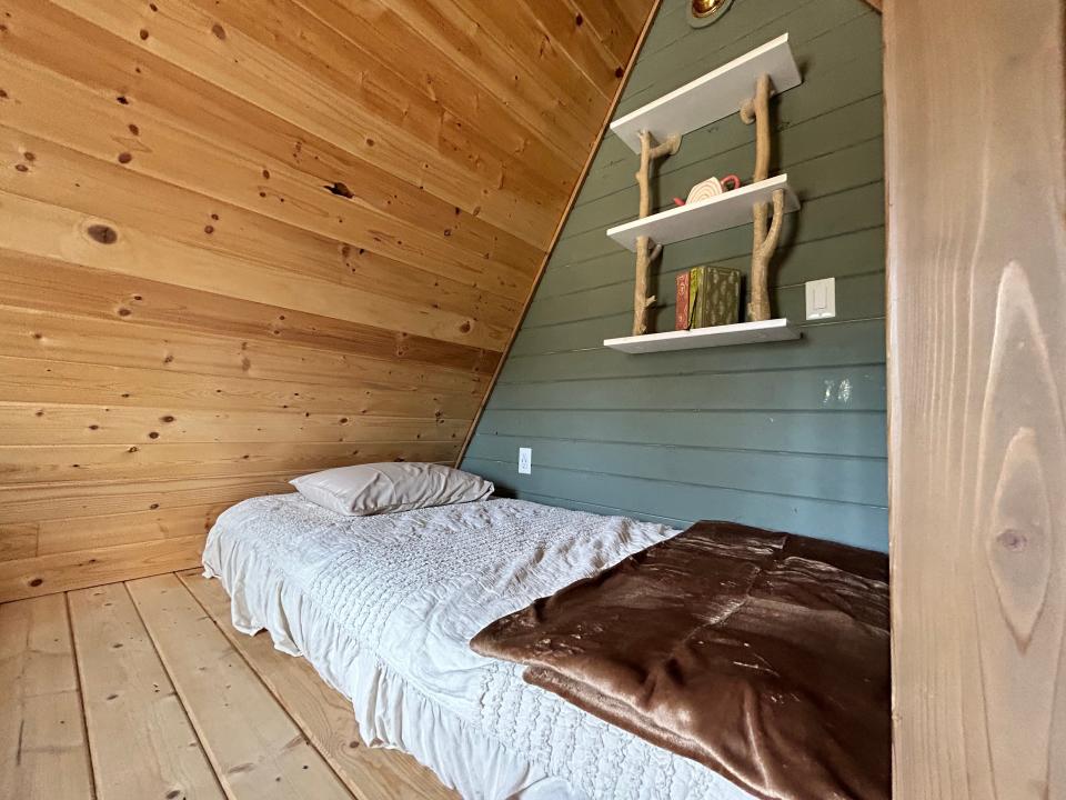 bed with bookshelf above it and wood slanted ceilings