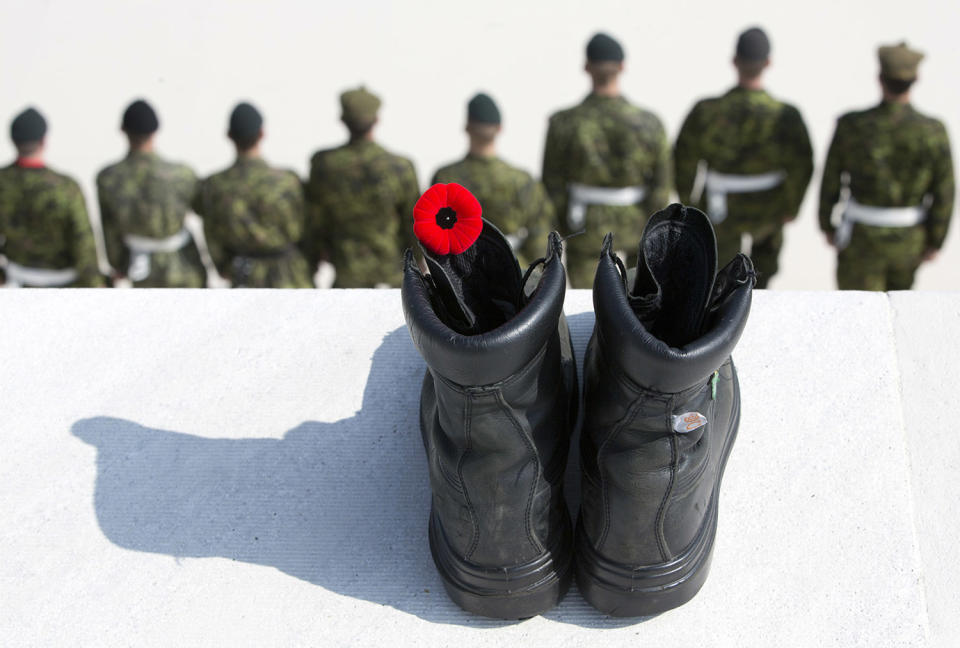 Soldiers stand in a line in front of a black boot with a red poppy