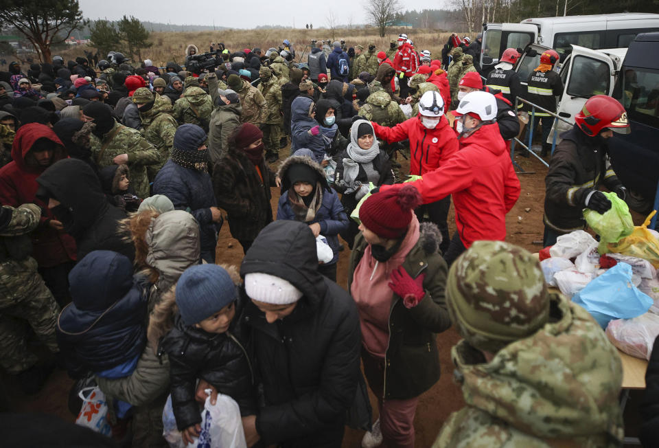 Belarusian Red Cross employees hand over humanitarian aid to migrants from the Middle East and elsewhere gathering at the Belarus-Poland border near Grodno, Belarus, on Tuesday, Nov. 16, 2021. The EU is calling for humanitarian aid as up to 4,000 migrants are stuck in makeshift camps in freezing weather in Belarus while Poland has reinforced its border with 15,000 soldiers, in addition to border guards and police. (Leonid Shcheglov/BelTA via AP)