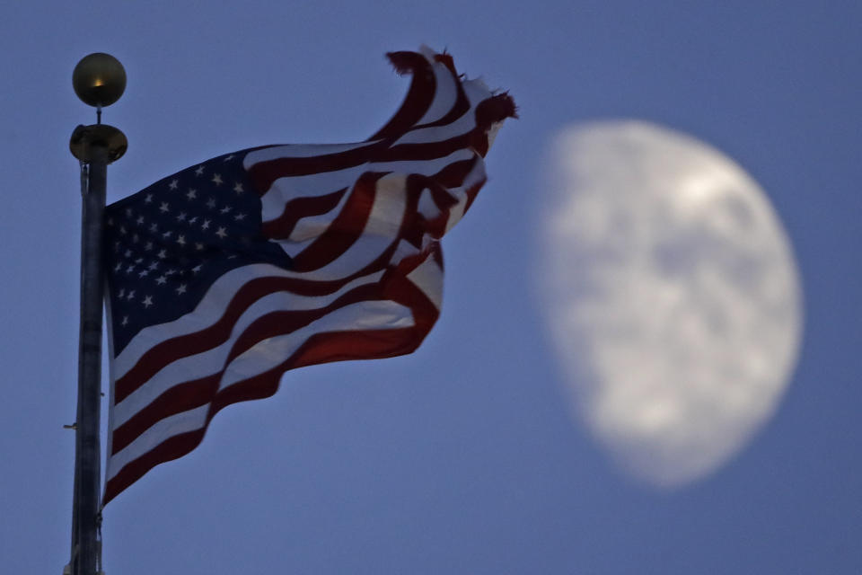 FILE - In this June 29, 2020, file photo, a flag flies in the wind above City Hall as the waxing gibbous moon passes behind clouds overhead in Kansas City, Mo. (AP Photo/Charlie Riedel, File)