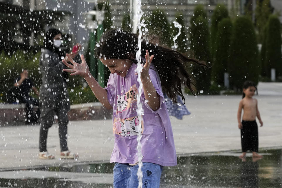 A girl enjoys a water fountain at the Ebrahim Park while temperature reaches 38 C (100.4 F) in Tehran, Iran, Tuesday, Aug. 1, 2023. Iran announced a nationwide two-day, Wednesday and Thursday, holiday because of increasing temperatures. (AP Photo/Vahid Salemi)