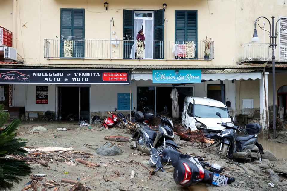 A woman looks from a balcony at a street covered in debris and damaged vehicles following a landslide on the Italian holiday island of Ischia, Italy November 26, 2022.