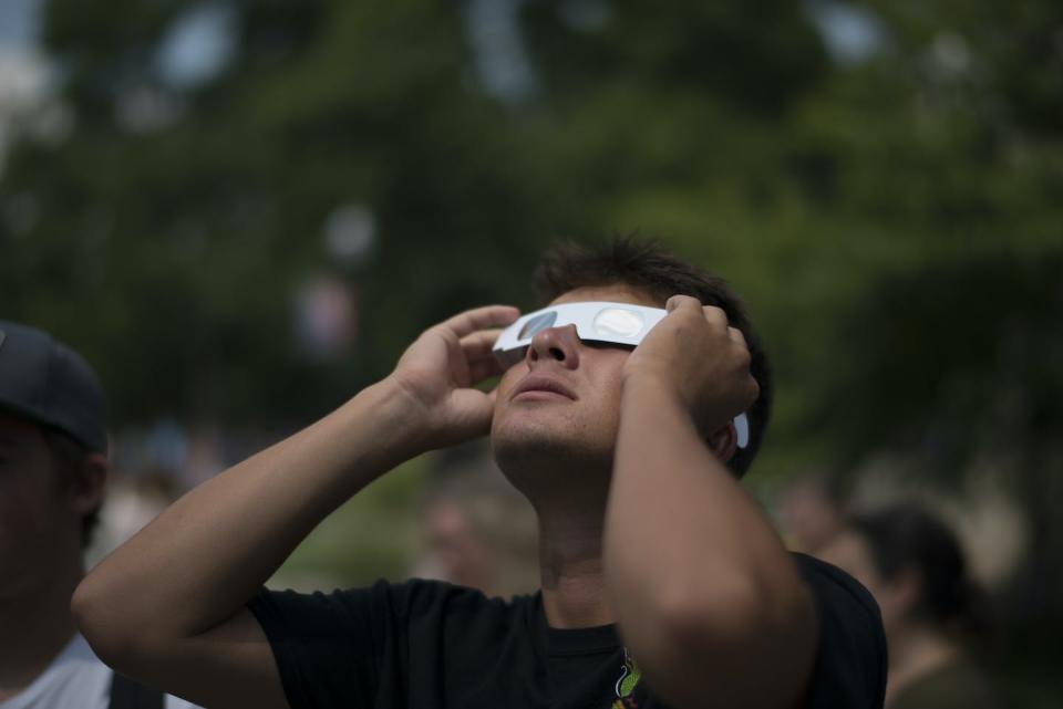 A man looking up at the sky, wearing gray paper eclipse glasses.