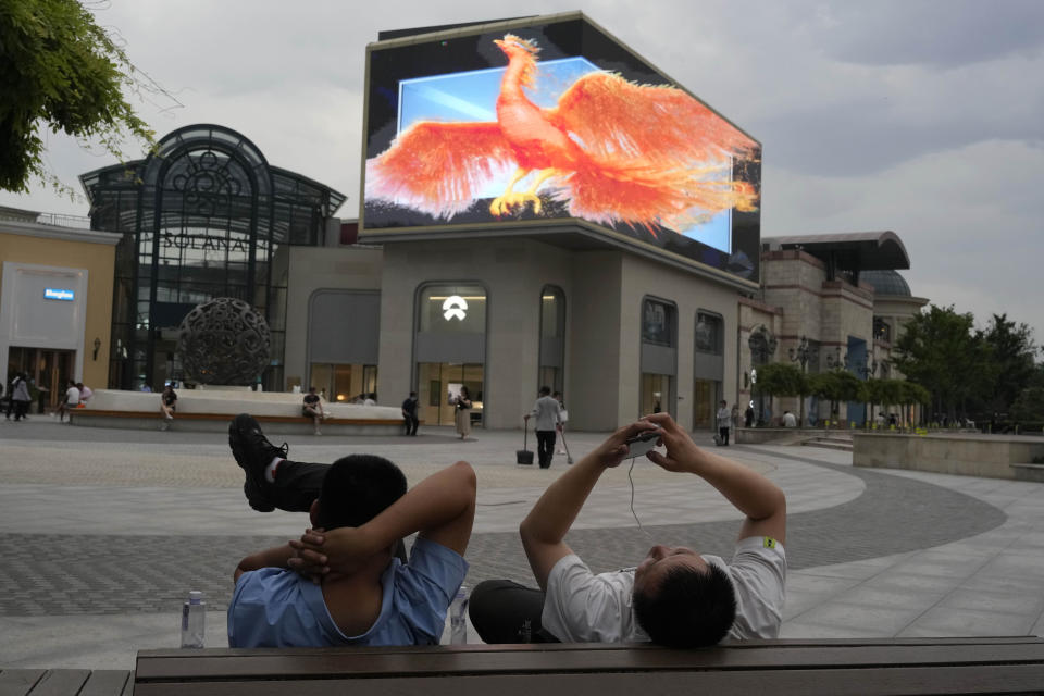 Chinese men rest near a screen depicting a phoenix at a mall in Beijing, on June 11, 2024. China kept a key lending rate unchanged on Monday, June 17, as data showed signs of persisting weakness in manufacturing and the real estate sector. (AP Photo/Ng Han Guan)