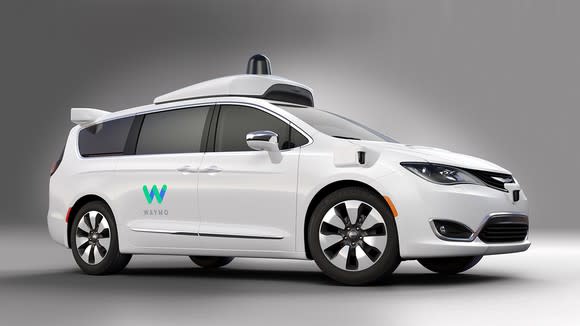 A white Chrysler Pacifica Hybrid minivan with Waymo logos and visible self-driving sensor hardware