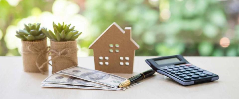 Home Loan, mortgage and real estate concept, House model with pile of dollar bills, calculator, pen and plant pots on table