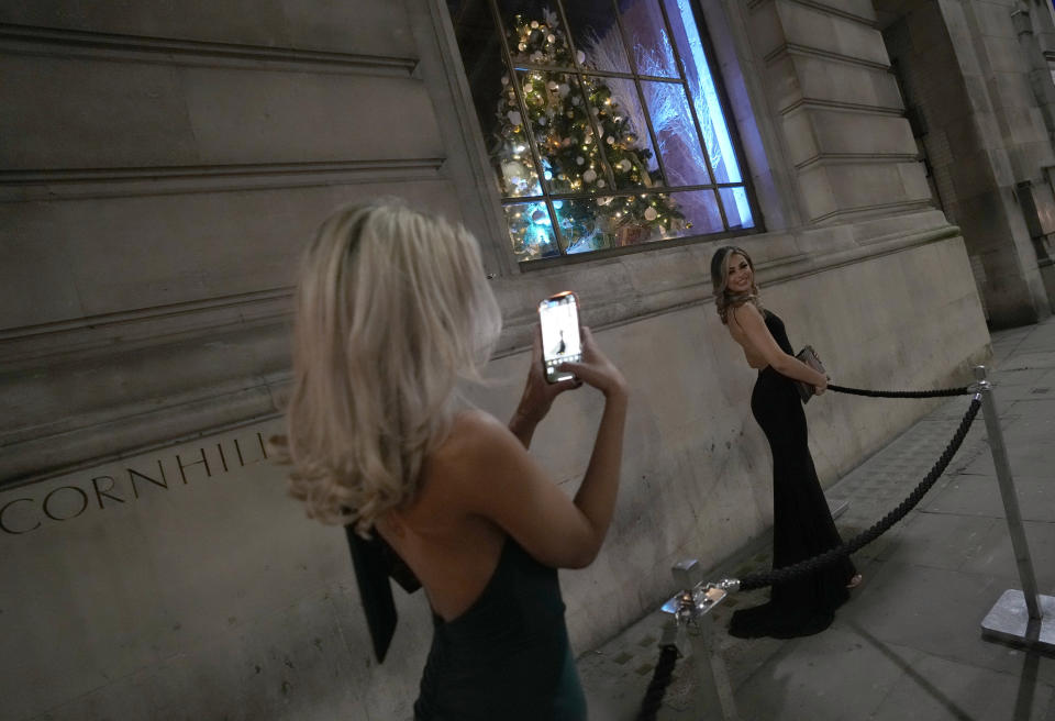 Two women dressed for a party take photos of each other outside a venue in London, Friday, Dec. 17, 2021. On what would normally be one of the busiest times for pubs and restaurants just before Christmas, customer numbers are down in central London due to concerns about the new omicron variant. Friday night in Central London was muted with one bar saying they have 30 customers inside when there should have been 170, with large amounts of cancellations in recent days. (AP Photo/Alastair Grant)