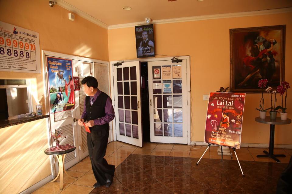 A man in slacks and button-down shirt walks near a set of double glass doors. Orchids sit on a small round table.