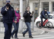 Polish police officer wearing a mask as he is taking on his radio while passers-by down ignore the requirement as Poland's authorities stepped up anti-COVID-19 measures after the nation registered three consecutive record numbers of new infections this week, in Warsaw, Poland, Friday, March 26, 2021.(AP Photo/Czarek Sokolowski)