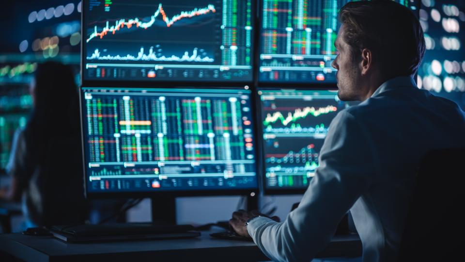 A closeup of a person reviewing graphs across multiple large computer monitors