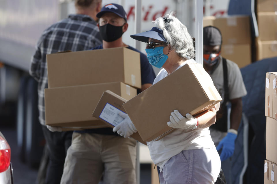 FILE - In this June 26, 2020, file photo, volunteers Juanita MacKenzie, front, and Dave Stutman carry boxes of food to a waiting car at a large mobile pantry set up by the Food Bank of the Rockies in the parking lot of Empower Field at Mile High in west Denver. In an effort to keep Colorado residents fed and employed this winter, Colorado's Legislature is concluding a special session Wednesday, Dec. 2, 2020, by passing bills offering assistance to restaurants and food pantries struggling to keep their doors open during the coronavirus pandemic. (AP Photo/David Zalubowski, File)