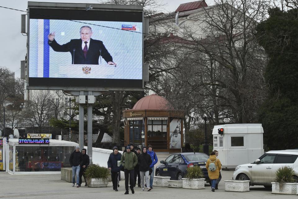 People walk in front of a TV screen n Sevastopol, Crimea, showing Putin during his state of the nation address.