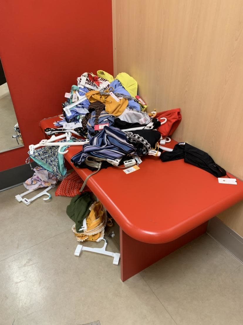 Clothes all over a fitting room in a big pile