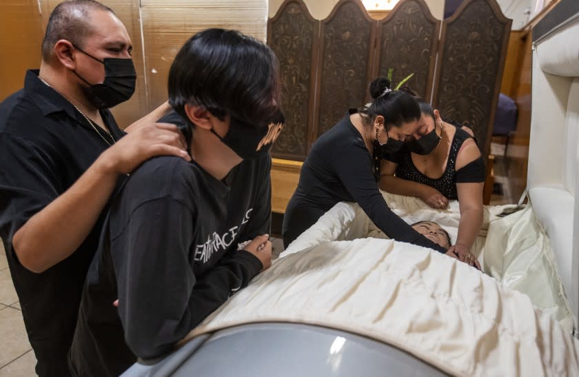 EAST LOS ANGELES, CA - DECEMBER 20: Sisters Dolores, right, and Dulce Chavez hold hands on their mother Edith Fernandez as Dolores' husband Antonio Elizalde and son Valentine, 12, wait alongside her casket at the Continental Funeral Home on Sunday, Dec. 20, 2020 in East Los Angeles, CA. The 47-year-old died Dec. 8, 2020 from complications of Covid-19. (Brian van der Brug / Los Angeles Times)