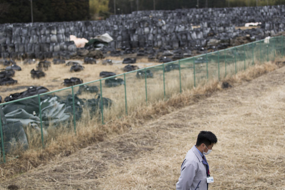 Yuya Hatakeyama, a Tomioka town official, walks by a temporary storage location for bags of dirt with possible radioactive waste during an interview with The Associated Press as he guides reporters in a "difficult-to-return" zone in Tomioka town, Fukushima prefecture, northeastern Japan, Friday, Feb. 26, 2021. Hatakeyama, forced to evacuate as a 14-year-old junior high school student, is back in town as a rookie official. Now at age 24, Hatakeyama wants to help rebuild the community and reconnect residents for the struggling town. (AP Photo/Hiro Komae)