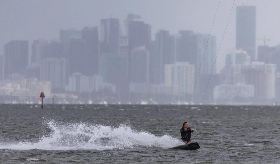 A kite boarder catches waves as rain makes its way over Brickell as seen from Matheson Hammock Park on Tuesday, April 11, 2023, in Coral Gables, Fla.