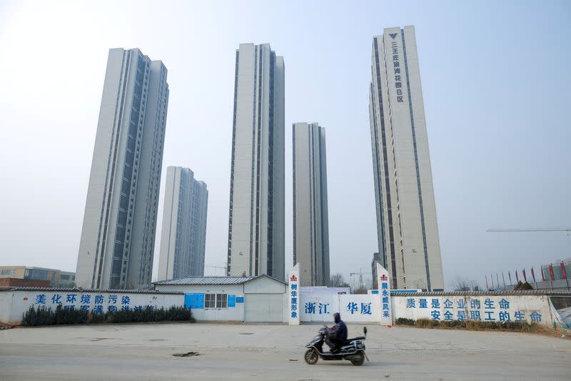 FILE PHOTO: A man rides a scooter past apartment highrises that are under construction near the new stadium in Zhengzhou