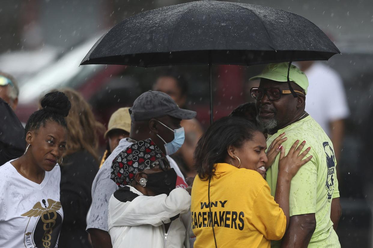 Bystanders gather under an umbrella as rain rolls in after a shooting at a supermarket on Saturday, May 14, 2022, in Buffalo, N.Y.