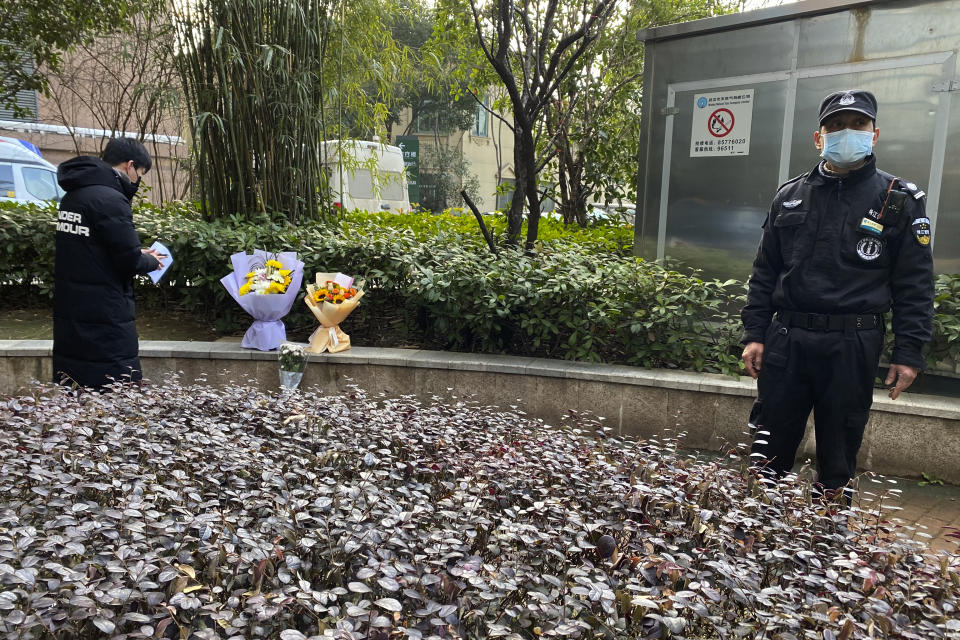 A security guard stands neaby as a man visiting the Wuhan Central Hospital leaves flowers in memory of Li Wenliang, the whistleblower doctor who sounded the alarm and was reprimanded by local police for it in the early days of Wuhan's pandemic, prior to the anniversary of his death, in central China's Hubei province, Saturday, Feb. 6, 2021. Dr. Li Wenliang died in the early hours of Feb. 7 from the virus first detected in this Chinese city. A small stream of people marked the anniversary at the hospital. The 34-year-old became a beloved figure and a potent symbol in China after it was revealed that he was one the whistleblowers who authorities had punished early for “spreading rumors” about a SARS-like virus. (AP Photo/Ng Han Guan)