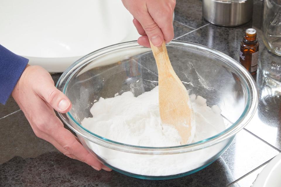 Woman using a wooden spoon to mix essential oils and baking soda.