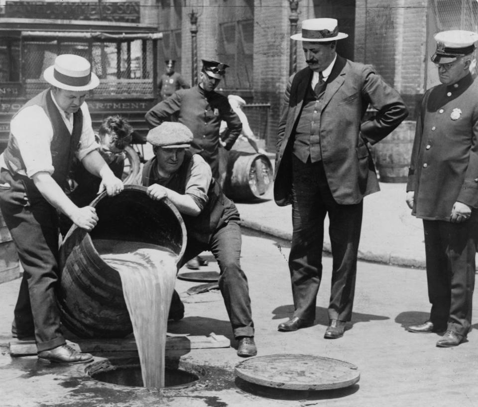 <p>New York City police officers supervise a pair of men as they dump a barrel of illegal alcohol into a sewer. Prohibition in the United States lasted from 1920 to 1933.</p><p>Related: <a href="https://www.esquire.com/lifestyle/g20969723/old-new-york-city-vintage-photos/" rel="nofollow noopener" target="_blank" data-ylk="slk:What New York City Looked Like the Year You Were Born;elm:context_link;itc:0;sec:content-canvas" class="link ">What New York City Looked Like the Year You Were Born</a></p>