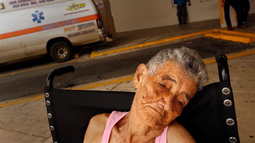 Una persona de edad avanzada en una silla de ruedas en el estacionamiento de un hospital en Puerto Rico