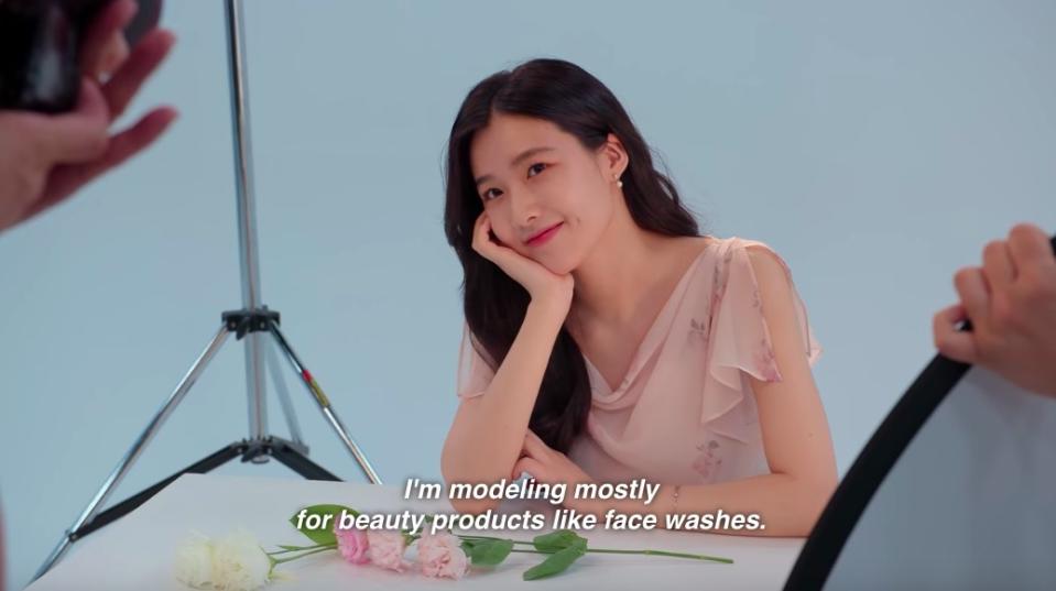 Su-min smiles angelically, posing for a photo, her voiceover says "I model mostly for beauty products like face washes"