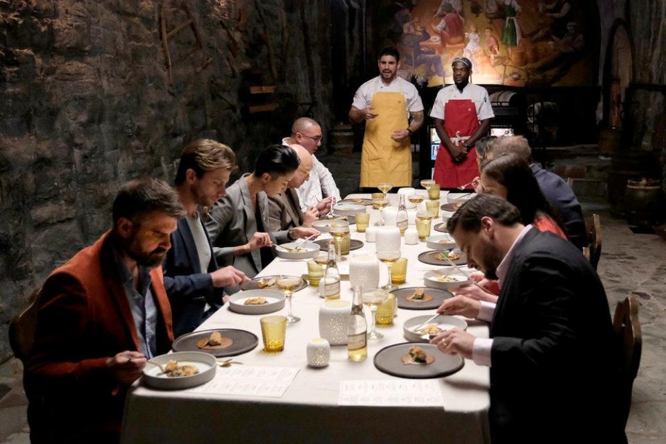 "Top Chef: Wisconsin" contestants Manny Barella, back left, and Charly Pierre serve their bar snack dishes to the 10 judges seated in the Historic Miller Caves in Milwaukee.