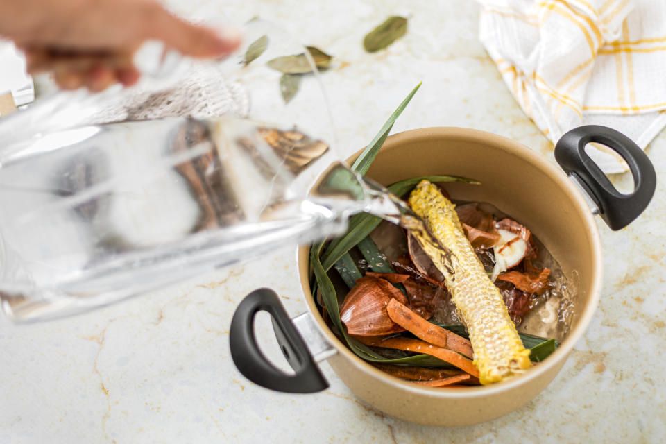 Person pours water into a pot with vegetable scraps for making broth