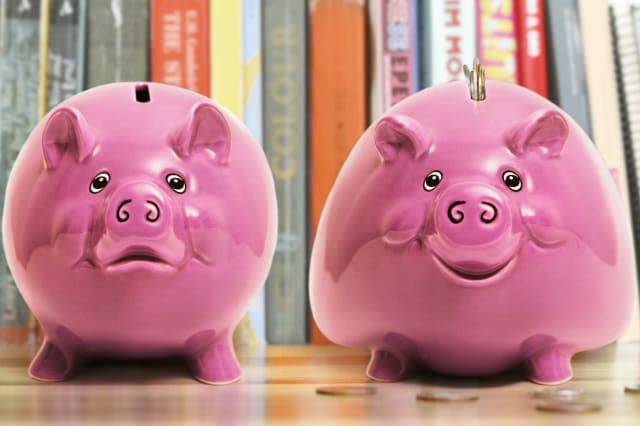 Two piggy banks, larger one with coins lodged in slot, smiling