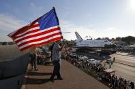 Roni Lopez, center, holds an American flag as the Space Shuttle Endeavour slowly moves along city streets on a 160-wheeled carrier in Los Angeles, Saturday, Oct. 13, 2012 towards the California Science Center museum. (AP Photo/Jae C. Hong)