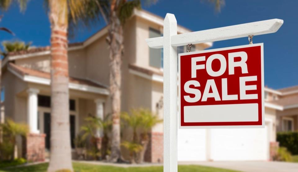 red and white house for sale sign in front yard of tropical home