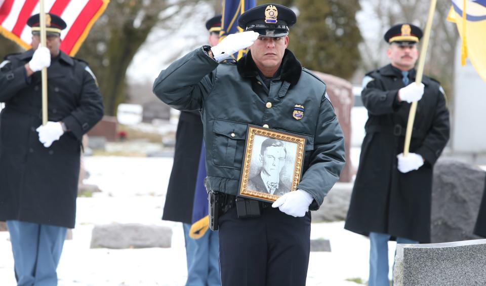 South Bend Police Patrolman Daniel Turner salutes and holds a photograph Wednesday, Jan. 10, 2024, at the grave marker dedication service for South Bend Police Officer Fred E. Buhland, who died in the line of duty 103 years ago — on Jan. 10, 1921 — and had been buried in an unmarked grave in Highland Cemetery.
